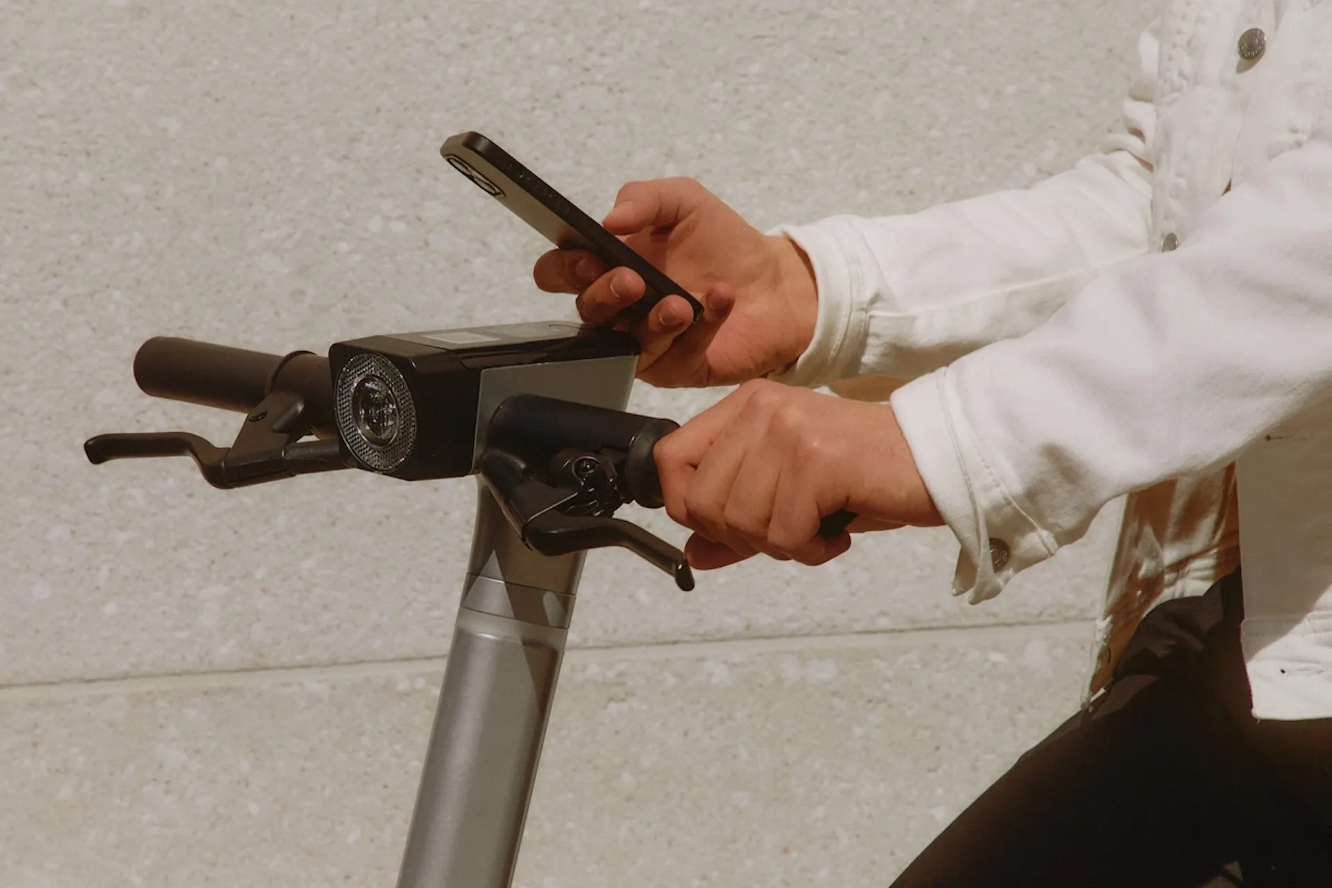 Person pushing an electic scooter while looking at their phone