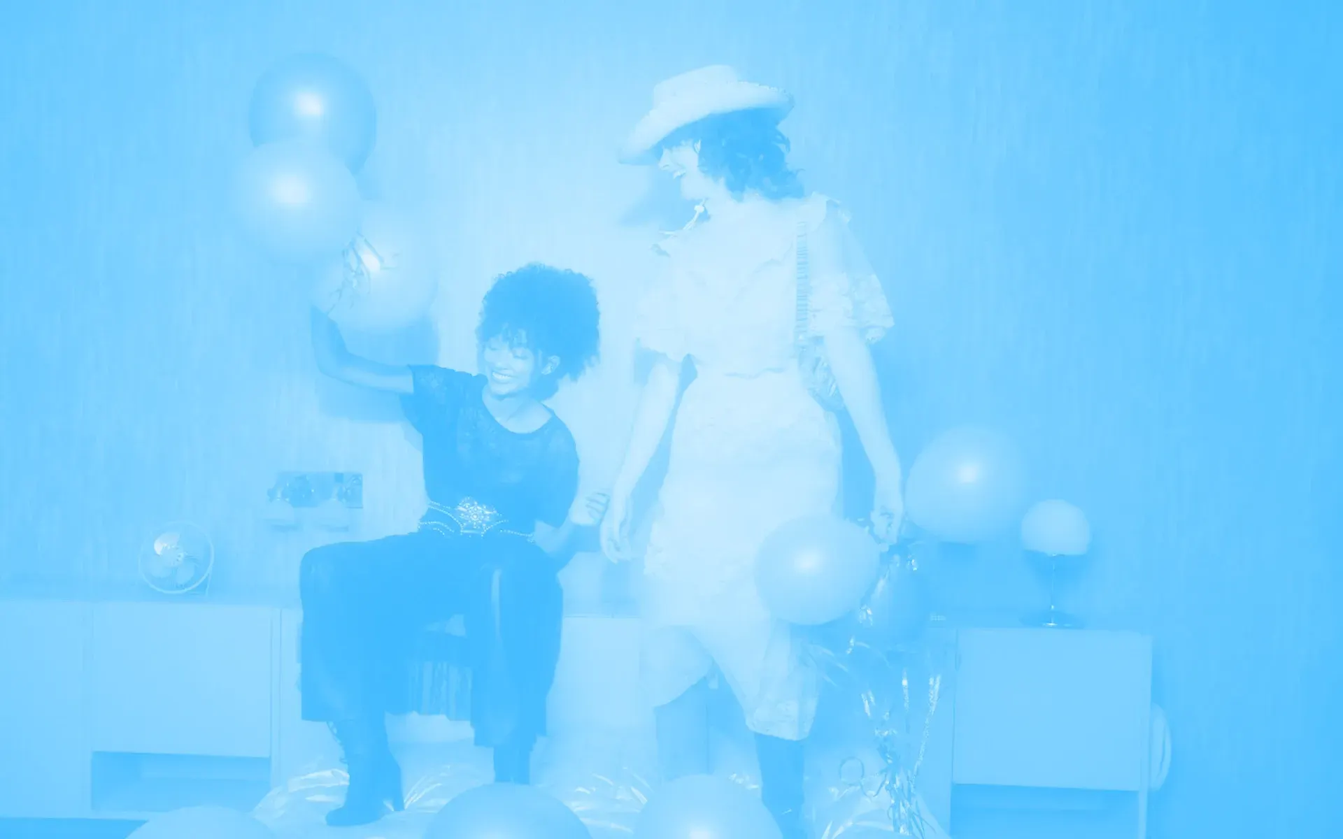 Two friends playing with balloons and laughing. One of them is wearing a cowboy hat