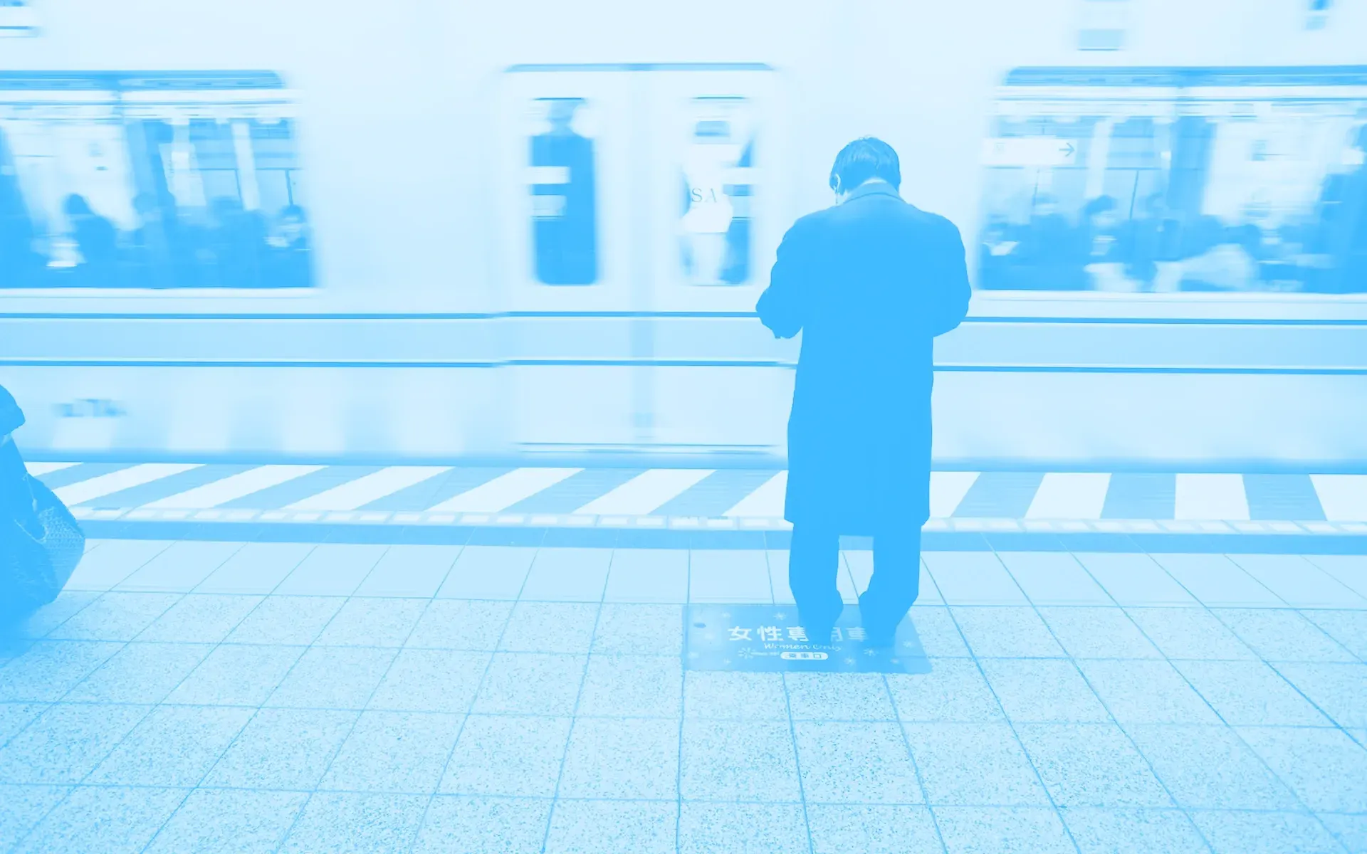 A person waiting for the subway and staring down at their mobile phone