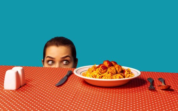 Woman hiding behind a bowl of spaghetti