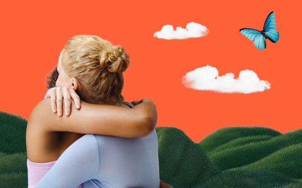 Two friends hugging in a field, with a butterfly flying overhead and hills in the background