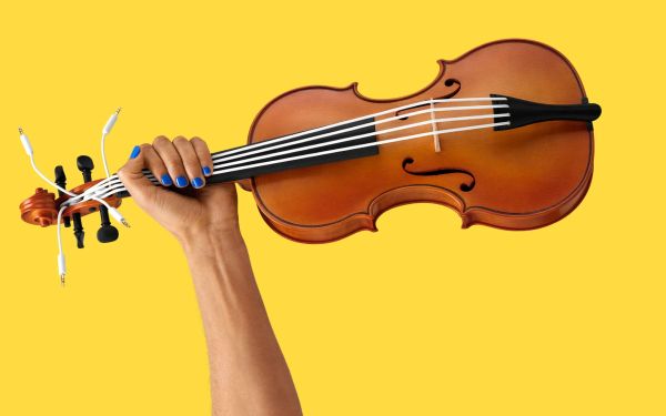 A hand holding a violin, which has strings made rom headphone cables