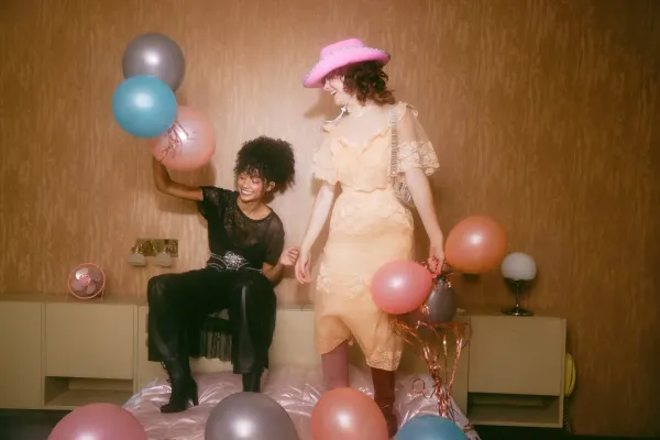 Two friends playing with balloons and laughing. One of them is wearing a pink cowboy hat