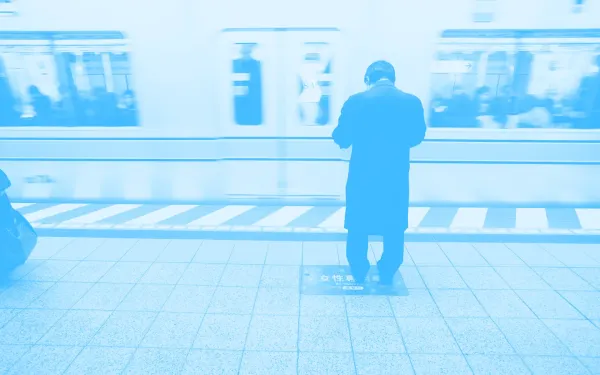 A person waiting for the subway and staring down at their mobile phone