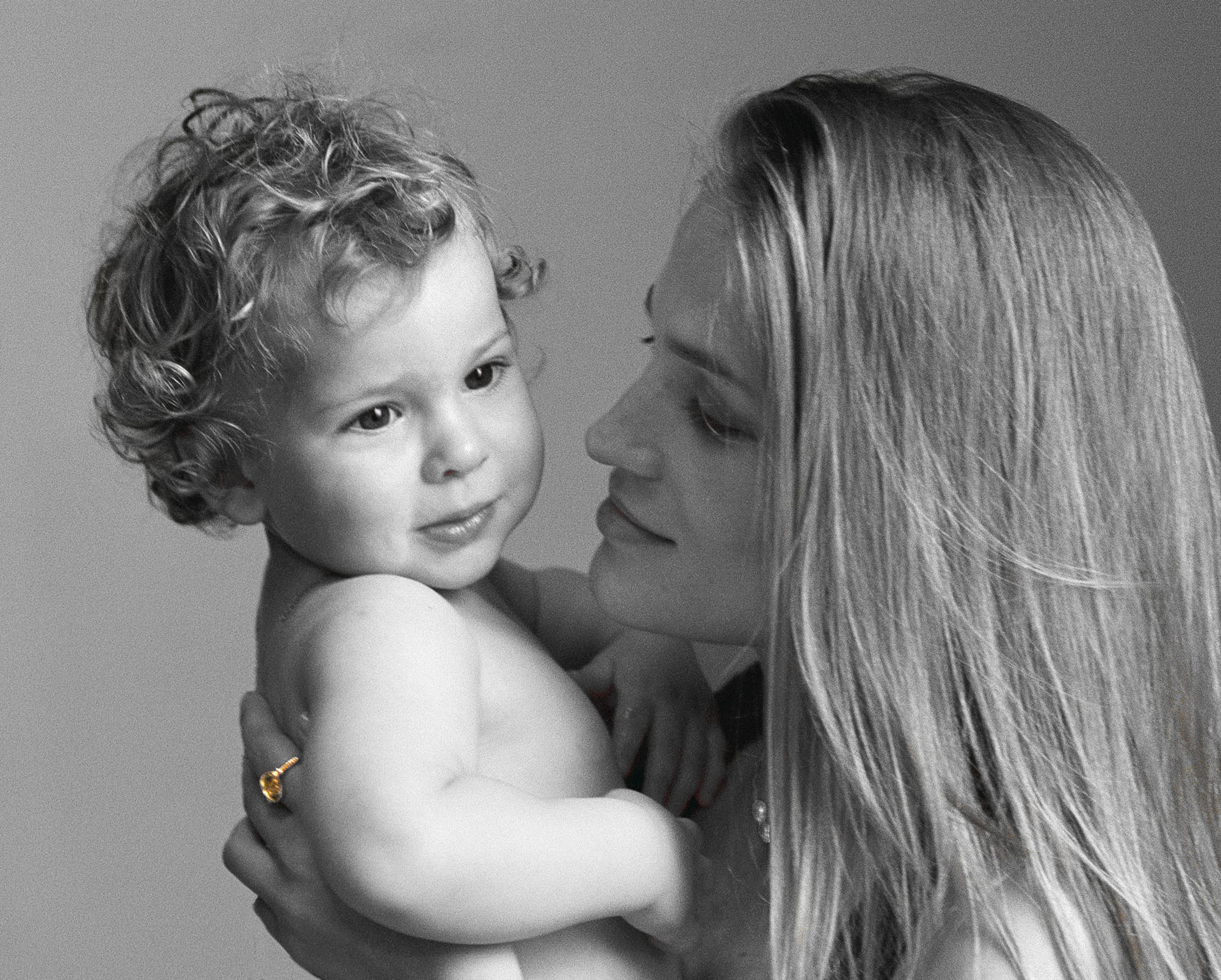 Mother holding child in Menē 24k gold jewelry from the 2026 Mother’s Day Collection.