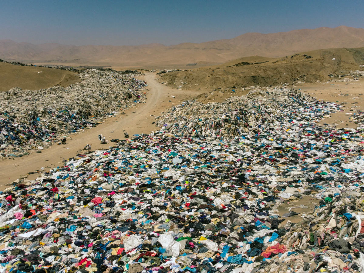 a vast desert landscape covered in mountains of discarded fast fashion clothing, illustrating global textile waste