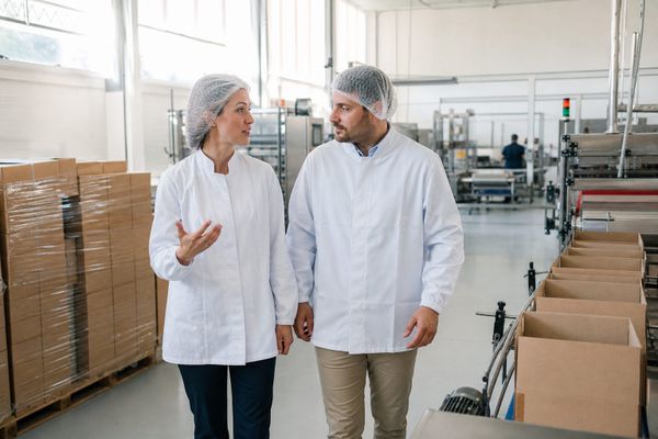 Recruitment consultant and operations manager discussing a role on a bright production floor