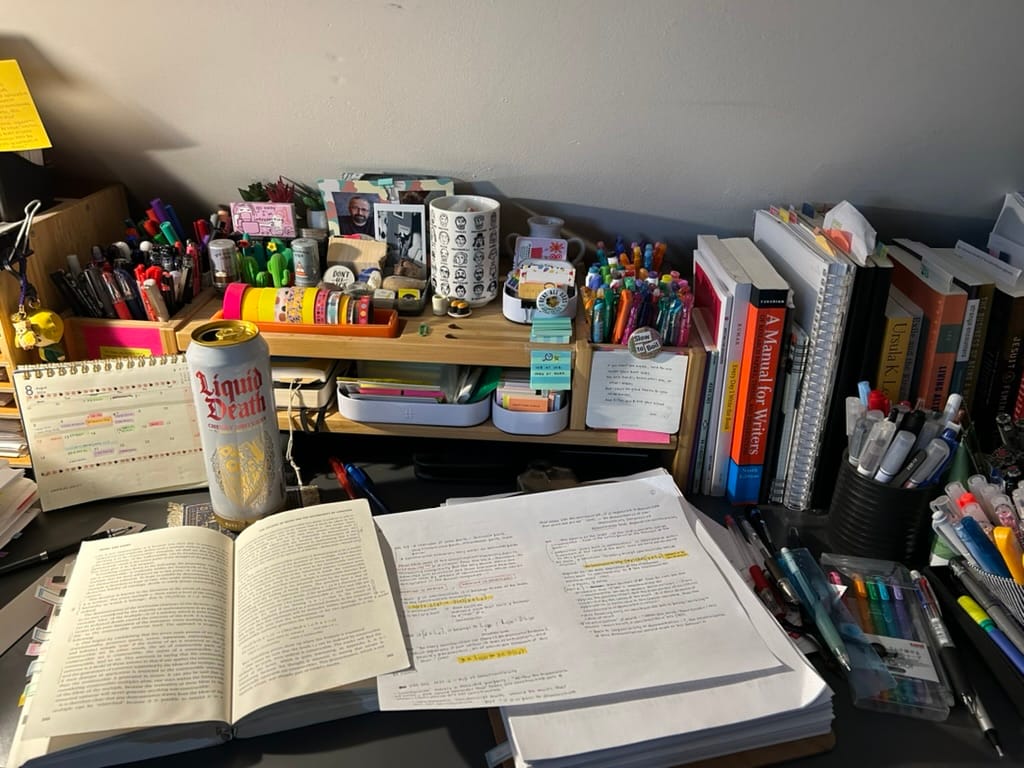 A desk piled with books and notes, surrounded by pens and washi tape.