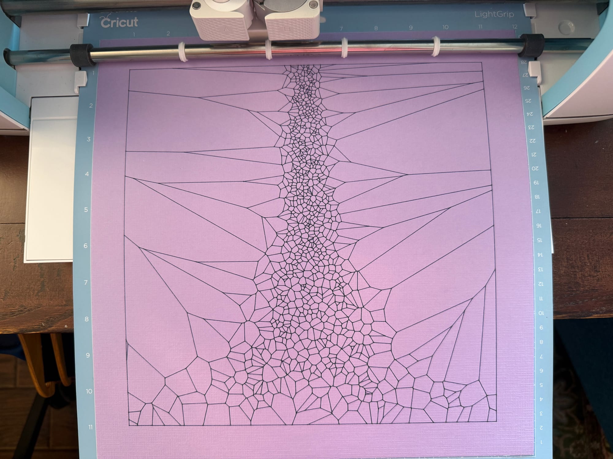 pen plotter output of voroni diagram with smallest cells down the center and expanding toward the bottom on purple paper coming out of a Cricut.