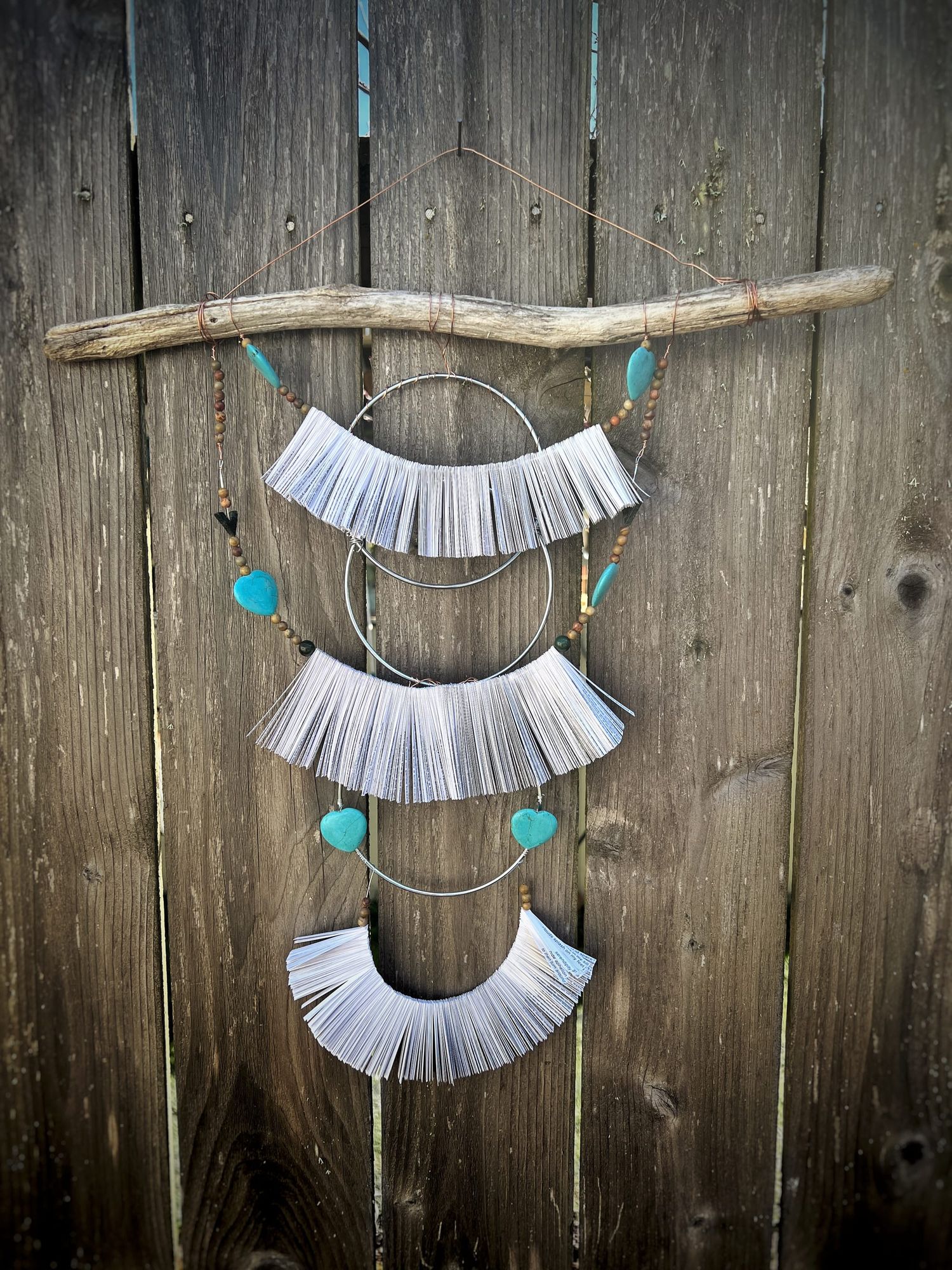 a work of art with a stick with 3 draping wires full of paper strips and beads