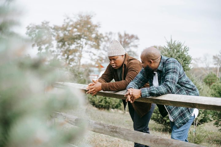 a father and his teenage son talking while leaning on a fence