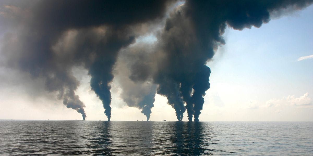 Multiple black smoke plumes are seen in the distance across open water