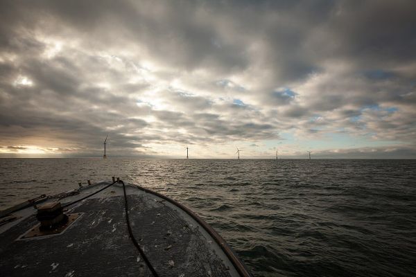 A view from a small boat heading toward five offshore wind turbines in the distance on a cloudy day.
