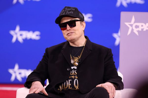 Elon Musk on stage at CPAC, wearing black and sunglasses and looking like an asshole