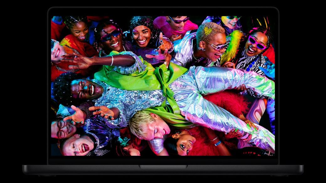 Apple's current MacBook Pro with M5 Pro and M5 Max, shown open from the front on a black background, its display filled with a colorful crowd of people in party outfits