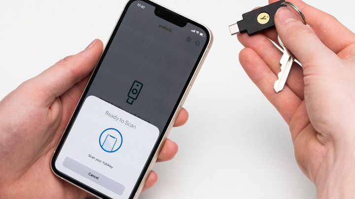 A hand tapping a Yubico security key against a phone