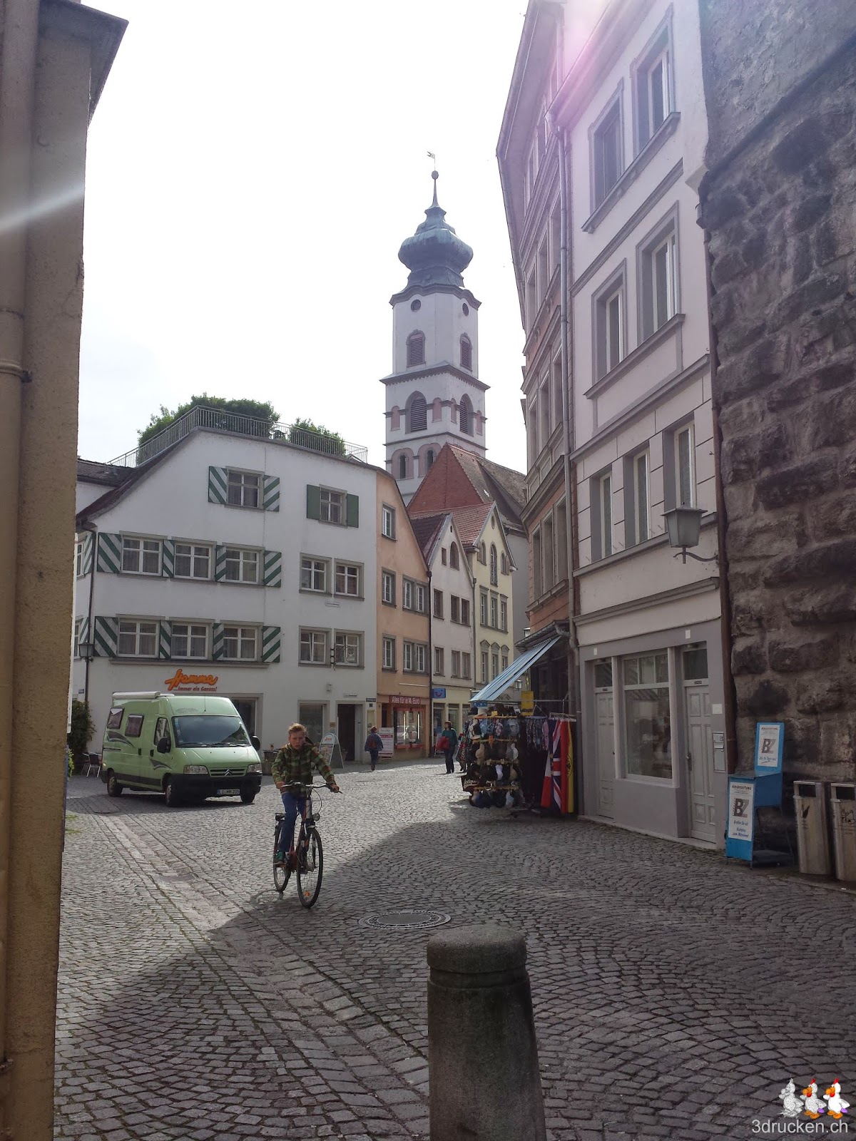 Foto in eine Gasse mit dem typischen Kopfsteinpflaster, im Hintergrund ein Kirchturm