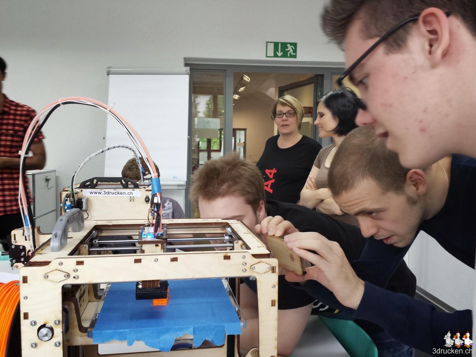 Foto einer Gruppe Lernenden mit Begleiter welche einen Druck am Ultimaker Original mit dem Handy filmen