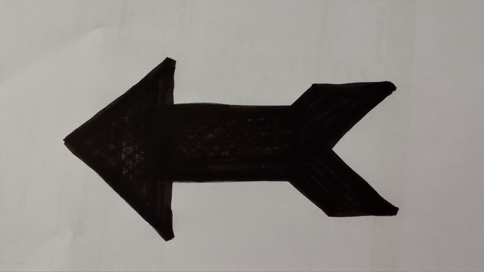 Foto einer mit schwarzem Filzstift gezeichneten Form eines Pfeils auf einem weissen Blatt Papier