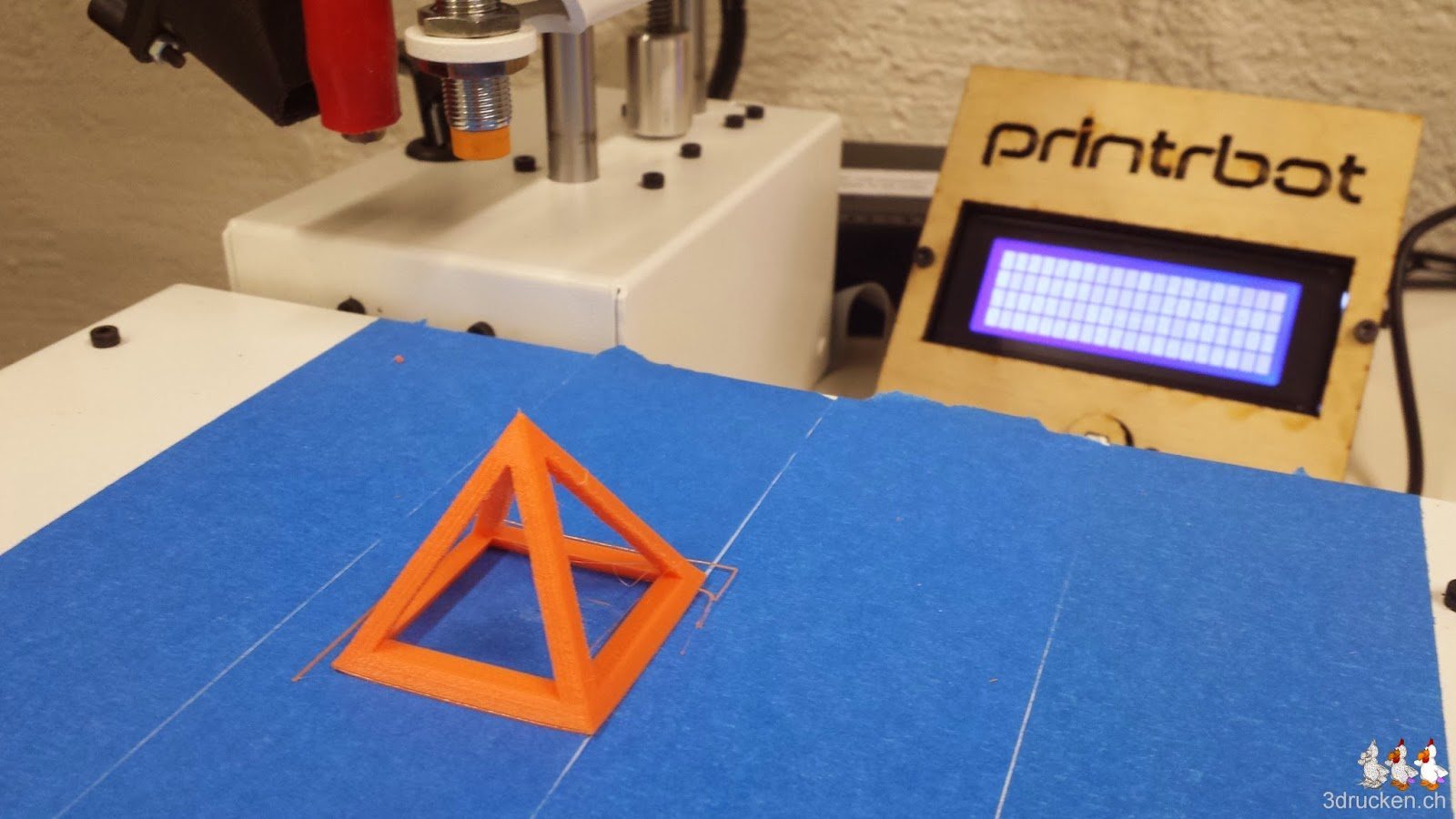 Foto des Drucktischs des Printrbot Simple Metal mit oranger Testpyramide darauf mit dem LCD mit schlechtem Betrachtungswinkel im Hintergrund
