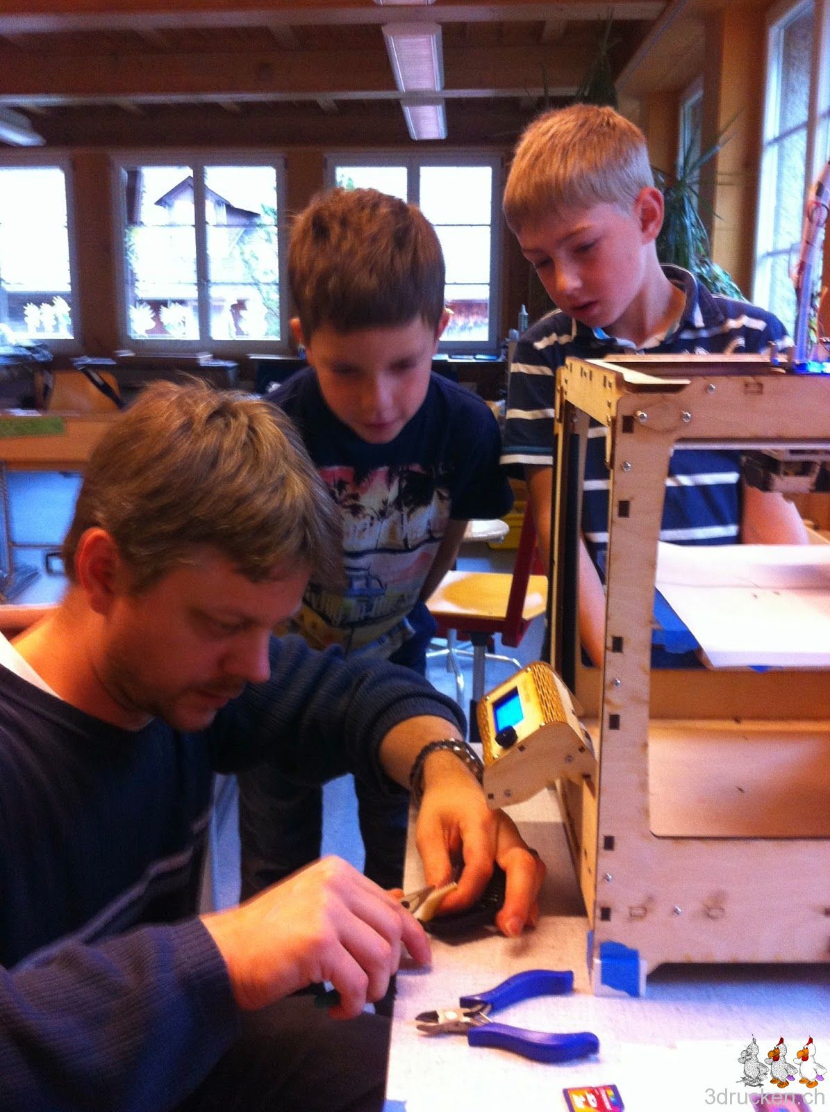 Foto von Gregor bei der Arbeit mit zwei Schülern als neugierige Zuschauer