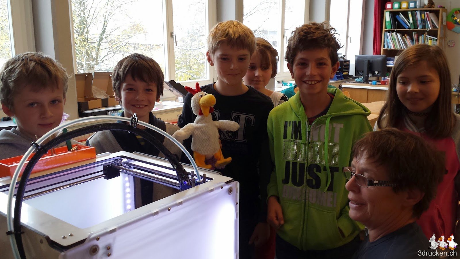 Gruppenbild am 3D-Drucker mit den Schülerinnen und Schülern, Uorschla und dem Güggel