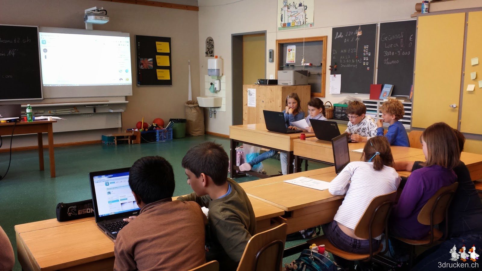 Foto vom Klassenzimmer mit den Schülerinnen und Schülern zu zweit an einem Notebook, vorne am Whiteboard das Beispiel aus Tinkercad