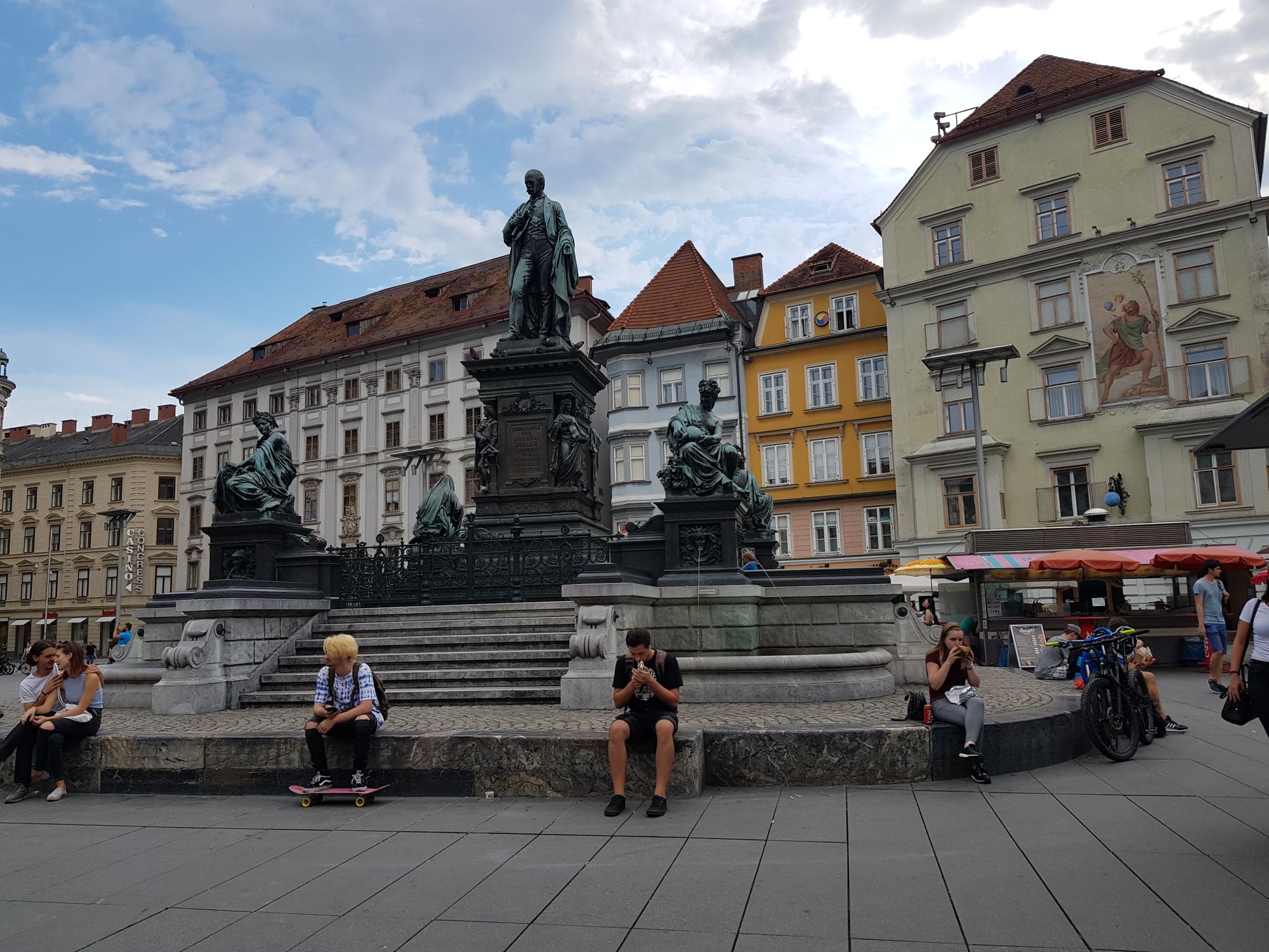 Erzherzog-Johann-Brunnendenkmal mit Leuten die auf der untersten Stufe sitzen. 
