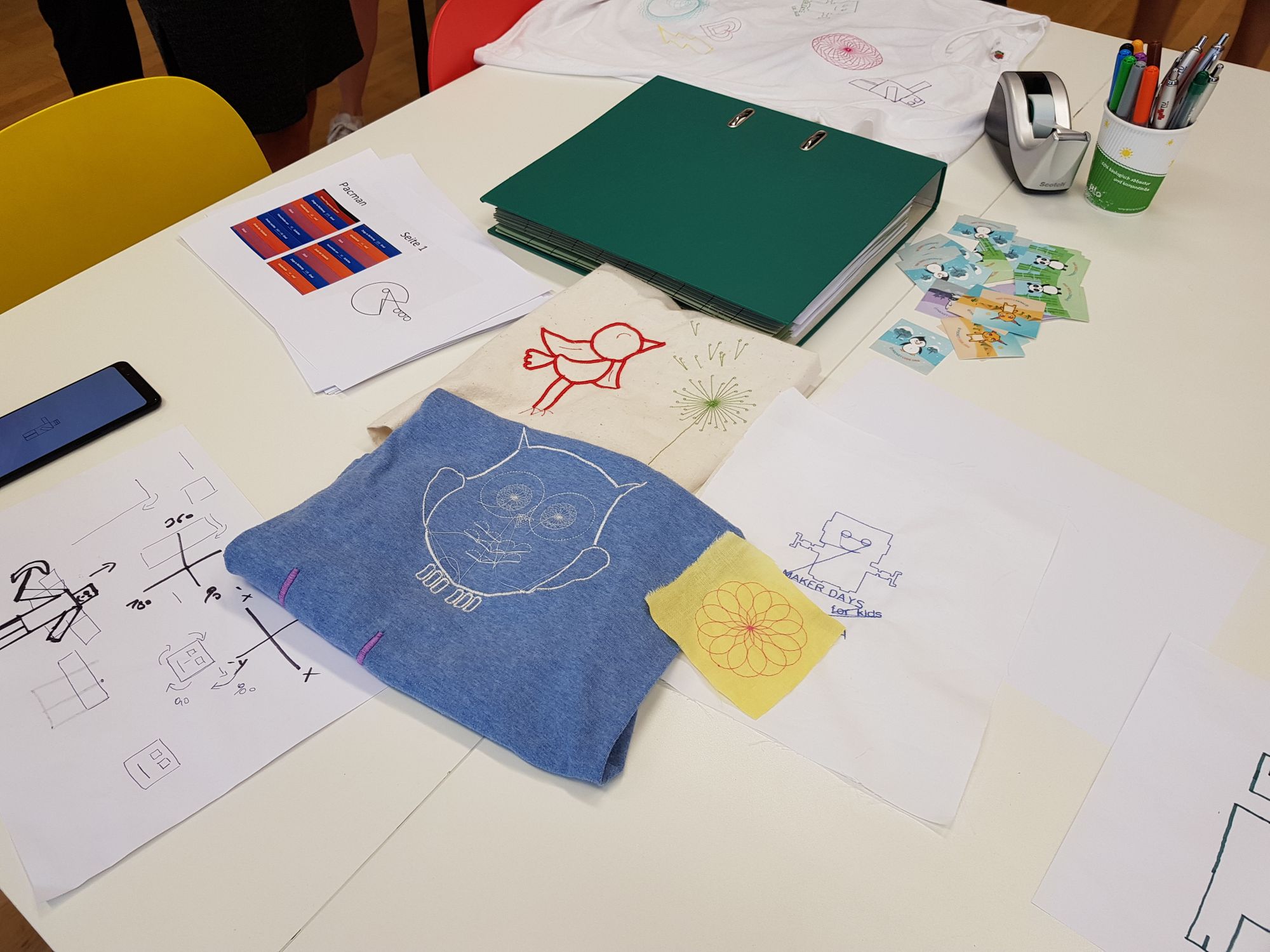 Ausgewählte Stickereiarbeiten und Skizzen auf dem Tisch. 