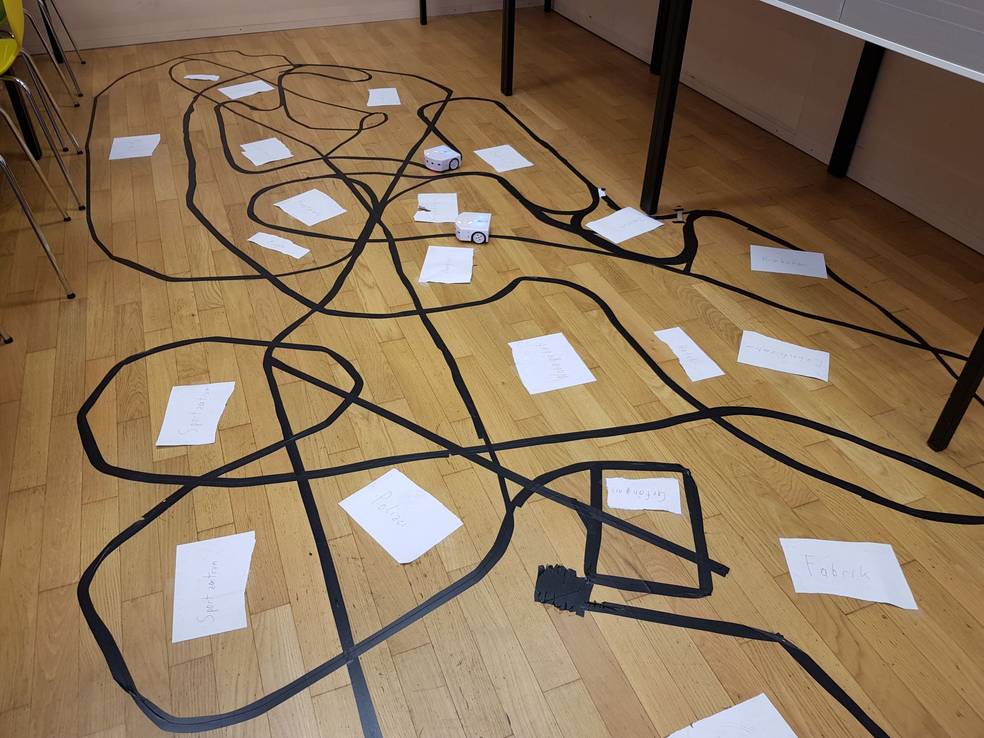 Mittels schwarzem Band geklebte Linien auf dem Boden, denen die Roboter folgen. 