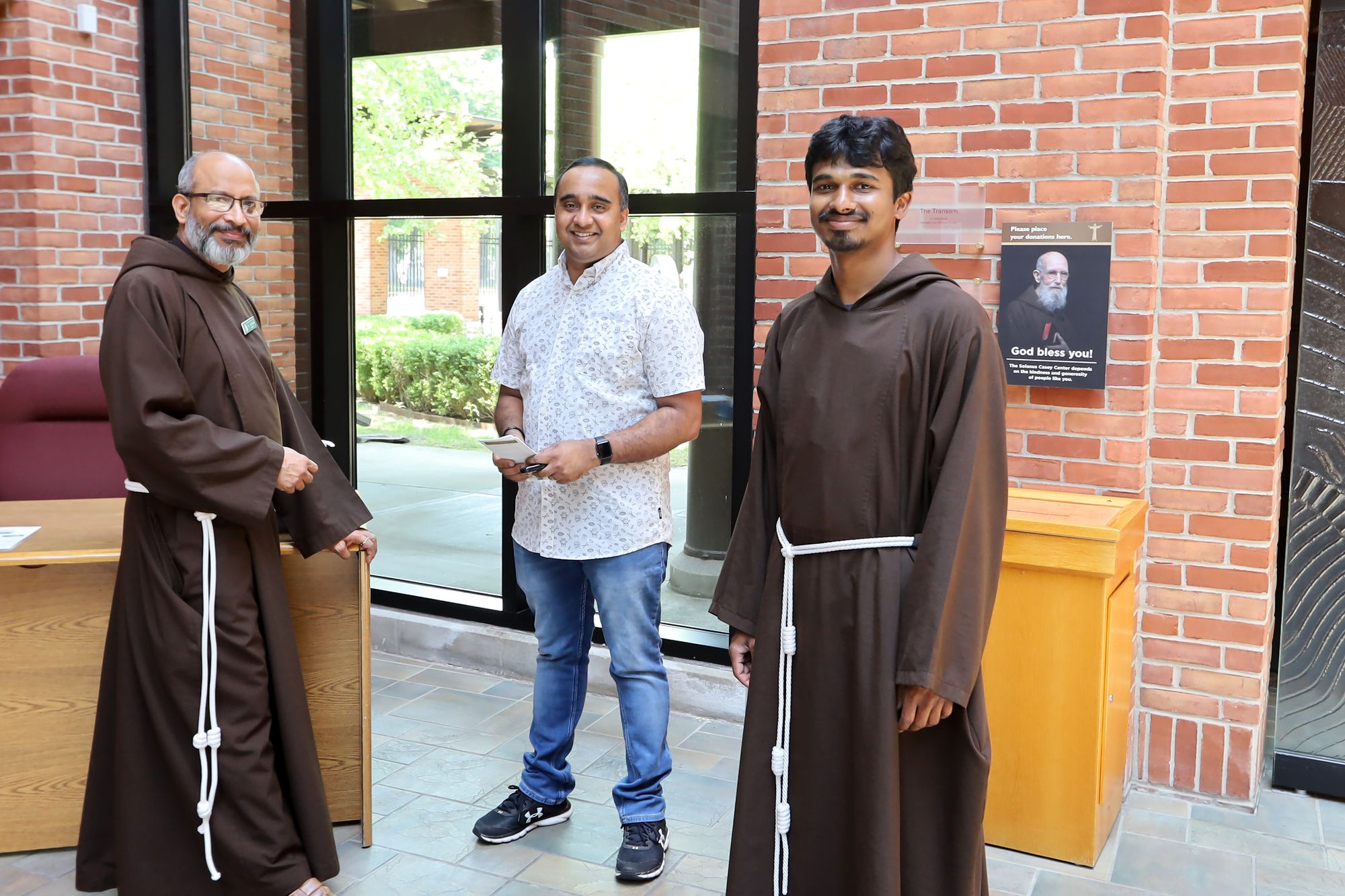 Br. George Kooran (L) and Br. Antony Julius Milton (R) greet a pilgrim at the Solanus Casey Center