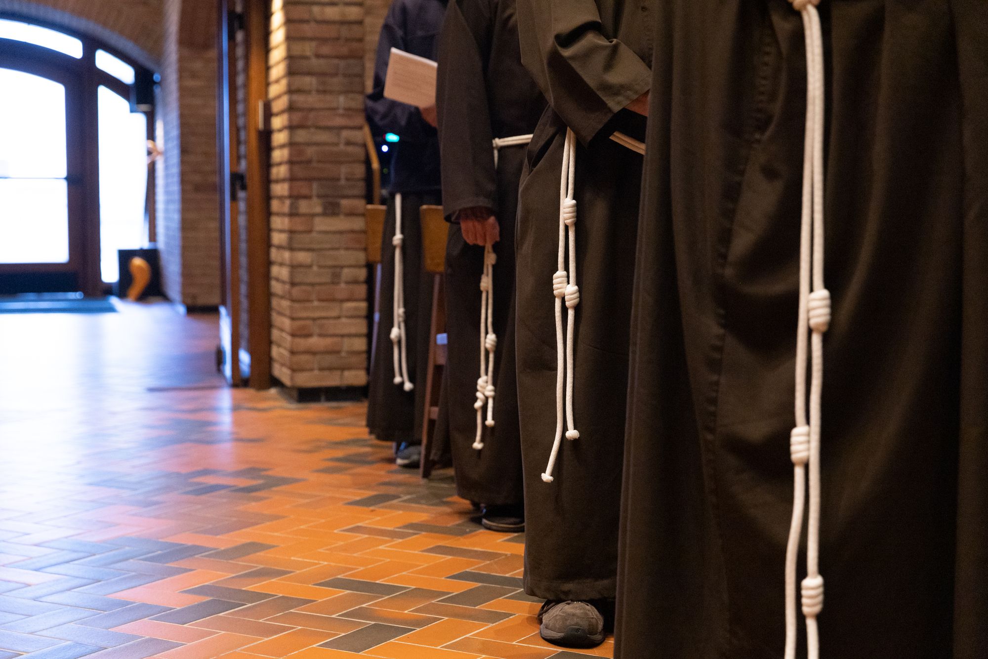 A cropped photo showing the lower half of friars standing in a chapel.