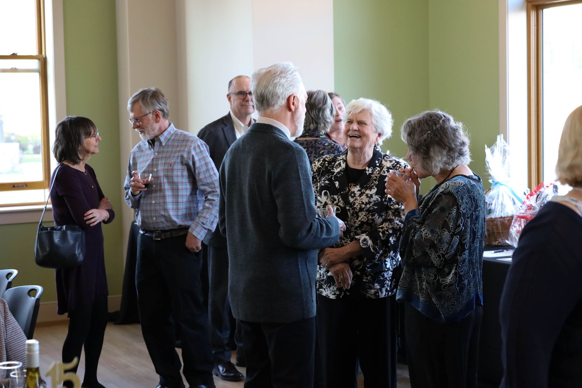 Color landscape photograph of Questors Club attendees chatting and hanging out near the silent auction tables.