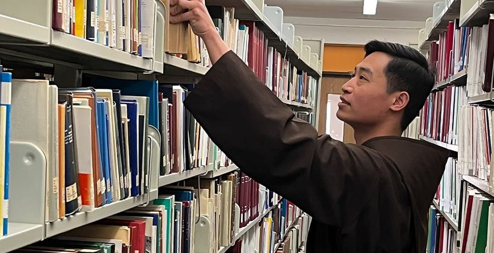 Br. Truyen pulls a book from the library stacks at St. Paul University.