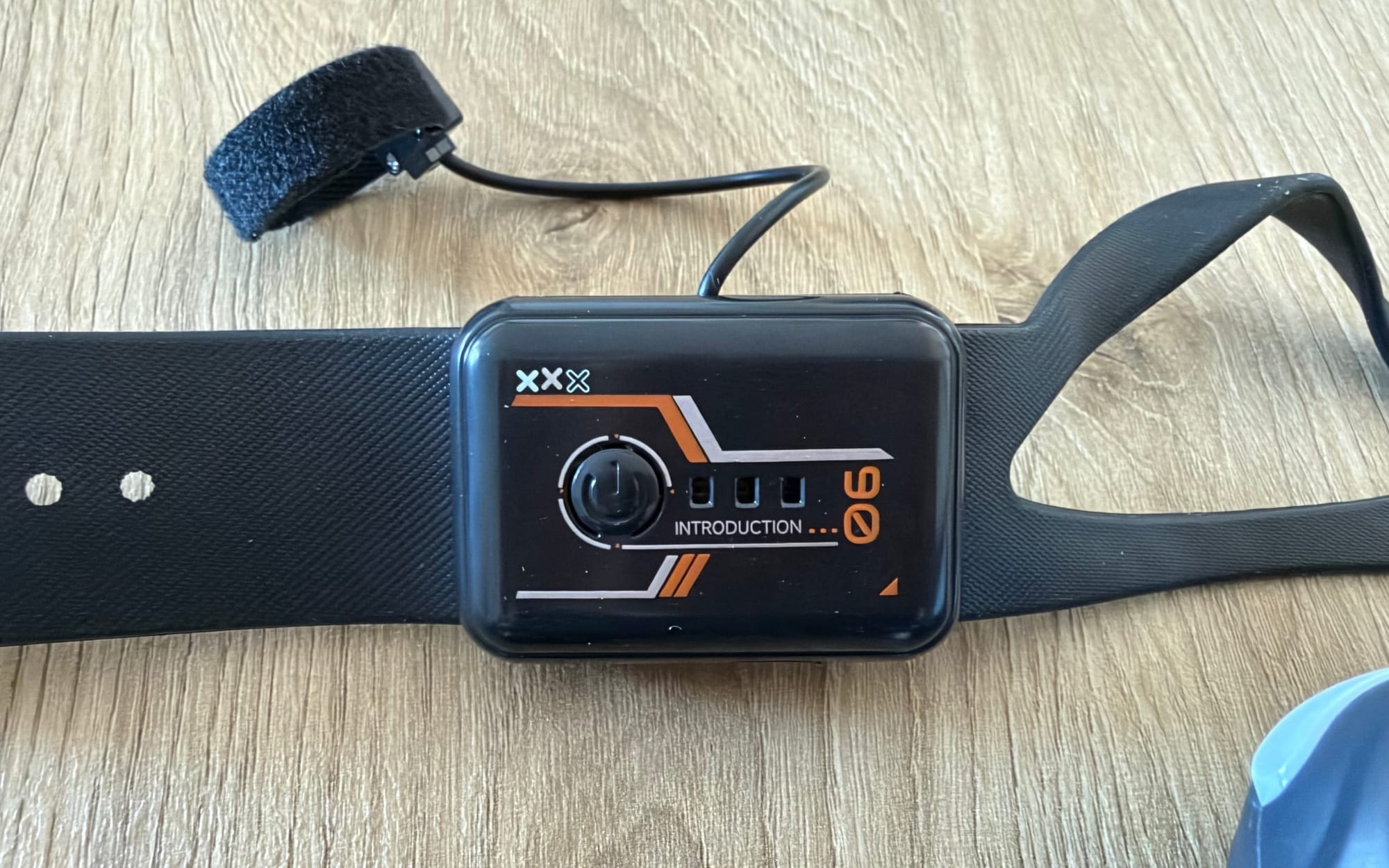 Ruko R1 gesture-control watch with its wrist strap and wired finger sensor on a wooden table.
