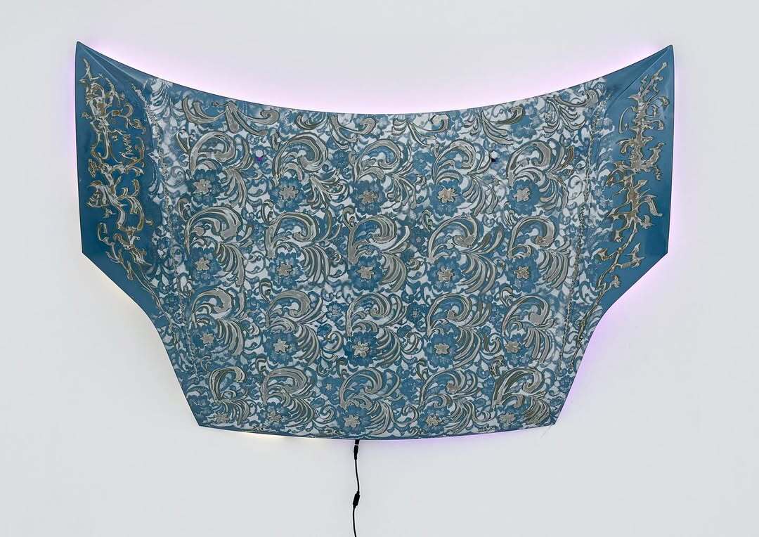 Installation view of Bety Krňanská’s artwork 'Bloomers,' a sculptural car hood covered in intricate floral patterns and backlit with soft light, exhibited at George Benias Gallery in Athens