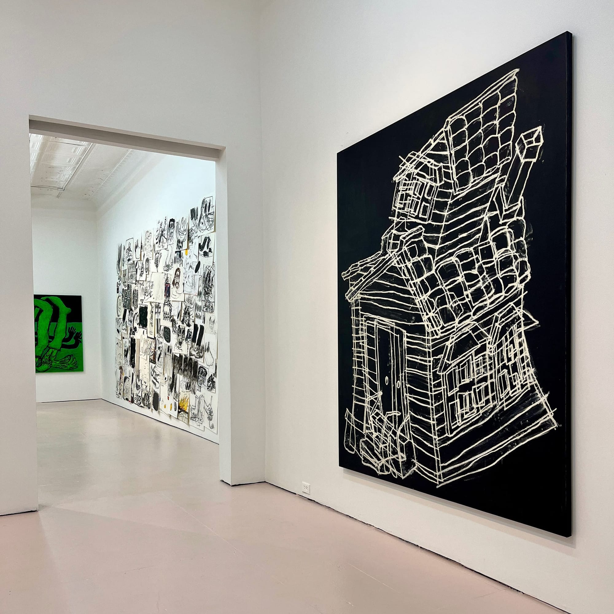 Exhibition view from As You Weren’t (2024) by artist Taylor A. White, showing three major wall pieces. On the right, a large black canvas features a white line drawing of a crooked, collapsing house. In the background, a salon-style wall is covered with dozens of expressive drawings and paintings on paper. A bright green painting with abstract black forms hangs on the far left wall. The gallery space is clean and minimal, with pale flooring and white walls