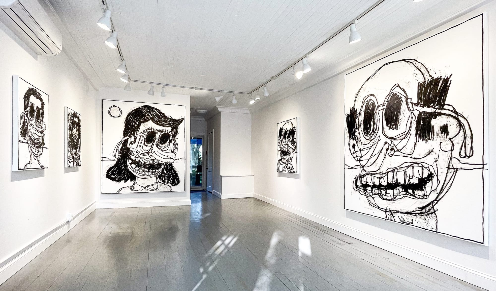 Gallery interior at Marquee Projects showing five large-scale black and white paintings by Taylor A. White. The works feature expressive, distorted cartoon-like faces with exaggerated eyes, mouths, and outlines. The exhibition is presented in a minimalist space with white walls, gray floors, and ceiling spotlights.
