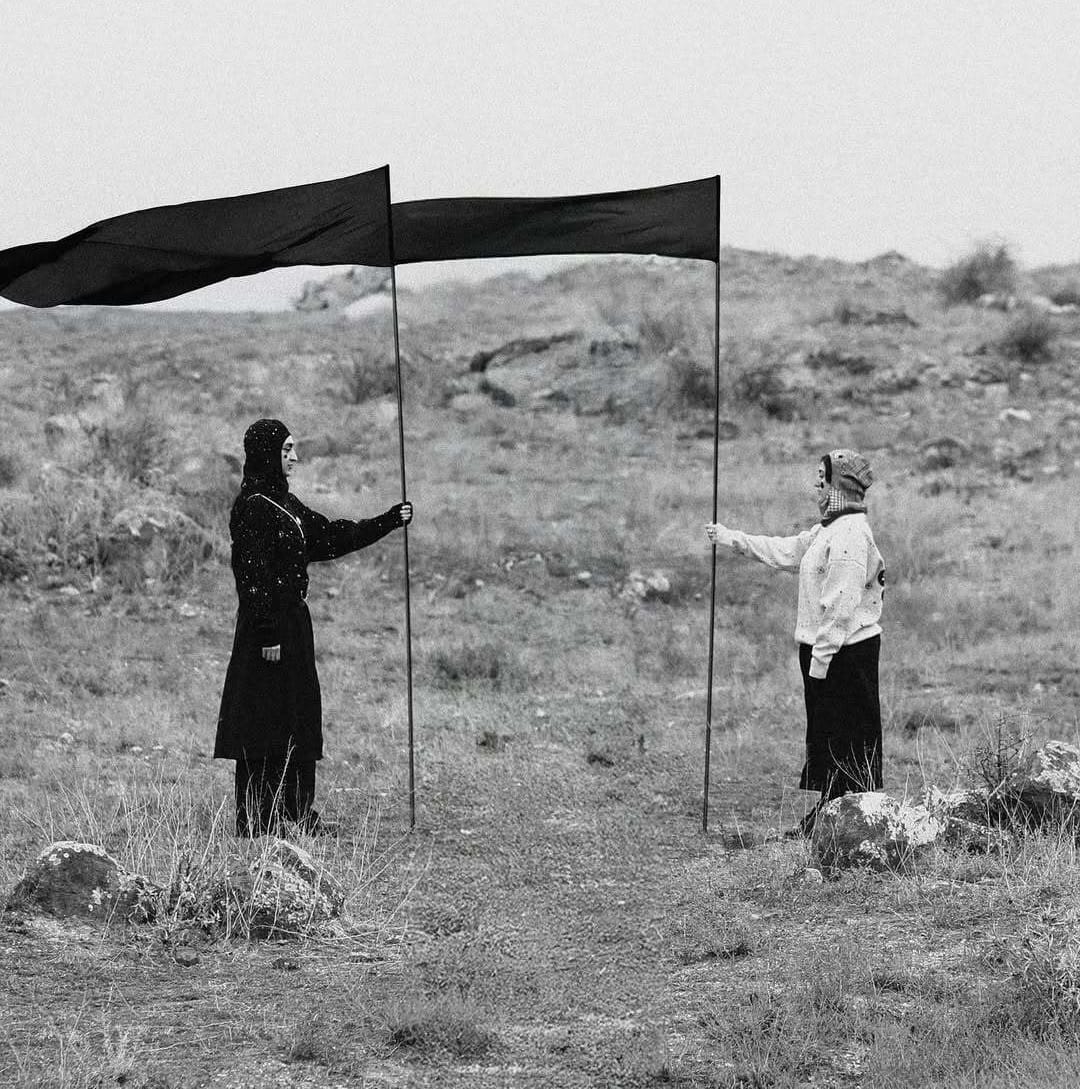 Khoren Matevosyan Emergence artwork, two figures holding black flags in a barren landscape, blending Armenian folklore, ritual, and performance.