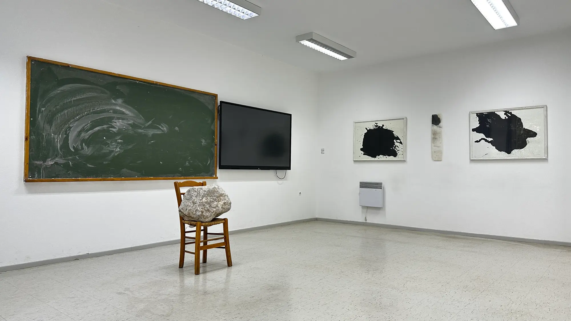 Exhibition view of Hydra School Projects 2025, Lithos Lethe. Jannis Kounellis’ stone-on-chair installation is shown opposite marble works by Brice Marden, forming a dialogue between Arte Povera and abstraction inside the former Hydra school building.