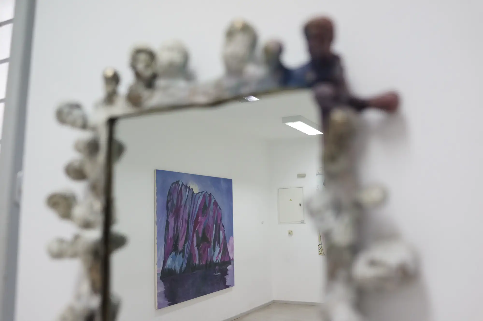 Exhibition view of Hydra School Projects 2025, Lithos Lethe. A bronze-framed mirror with small sculpted heads by William Farrell reflects a painting by Konrad Zukowski inside the Hydra school building.
