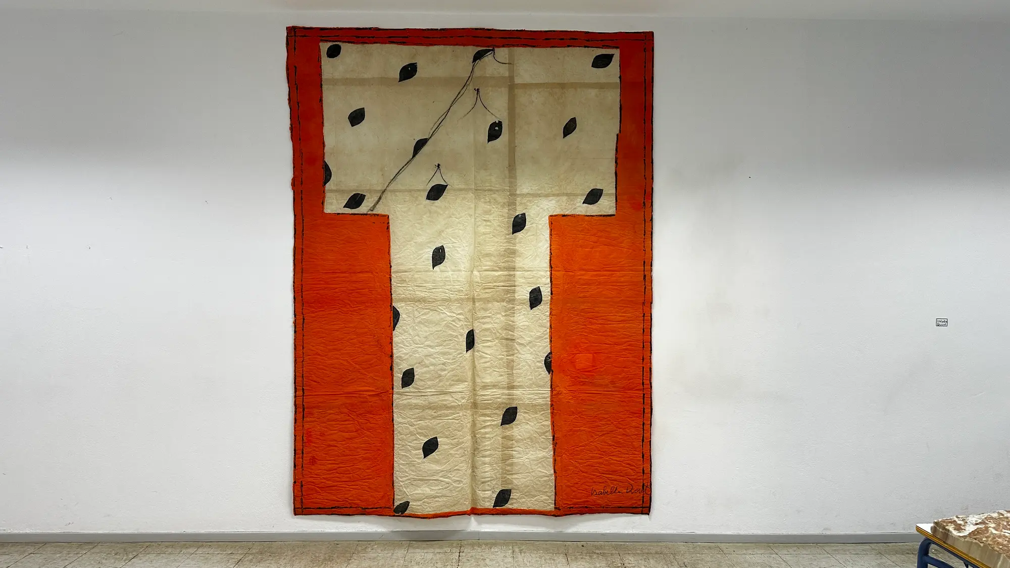 Exhibition view of Hydra School Projects 2025, Lithos Lethe. Textile work by Isabella Ducrot featuring stitched fabric panels with orange borders and black leaf-like patterns, installed in the former Hydra school building, Greece.