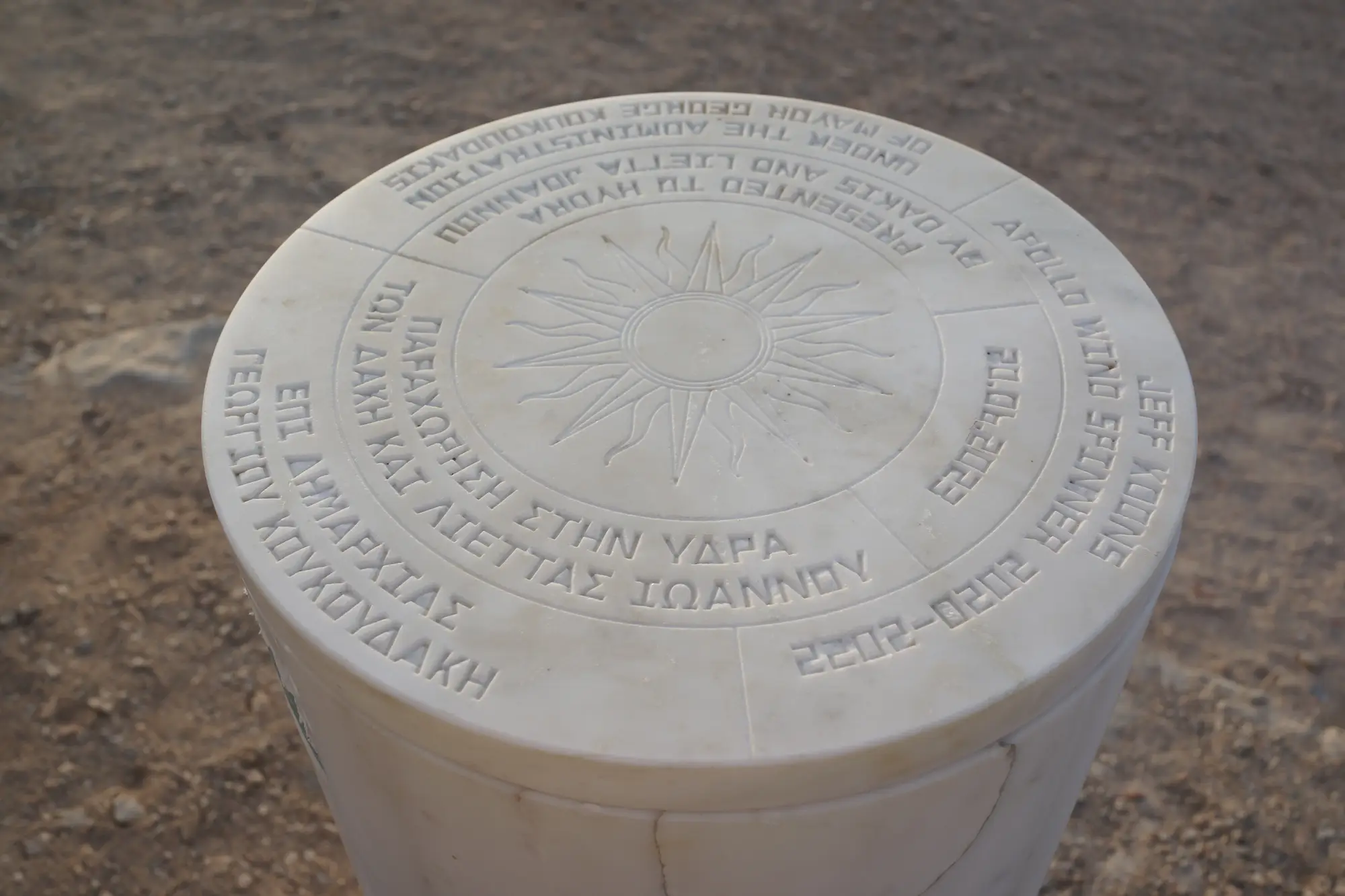Marble plaque for Jeff Koons’s “Apollo Wind Spinner” at DESTE Foundation, Hydra, Greek and English inscription noting gift by Dakis and Lietta Joannou under Mayor Georgios Koukoudakis, sun emblem engraved on top.