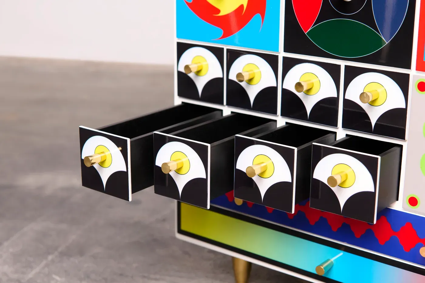 Kumkum Fernando – Detail of multiple small open drawers in the 27th Century Collector’s Cabinet, black-and-white fronts with yellow circles and brass handles, merging geometry with functional design.