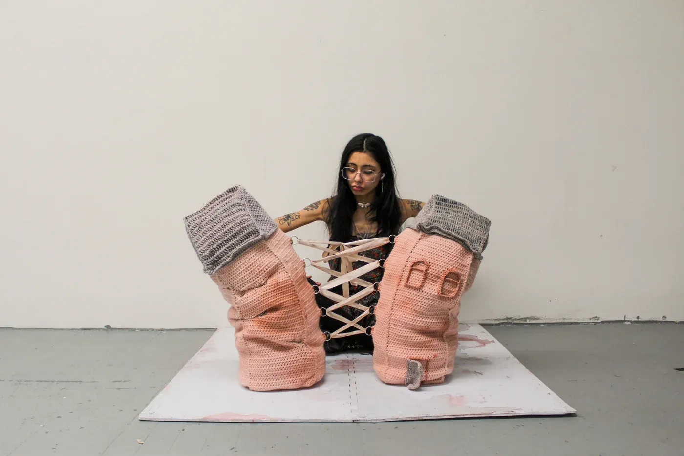 Ophelia Arc seated between two large crocheted pink and gray textile sculptures laced together with ribbons