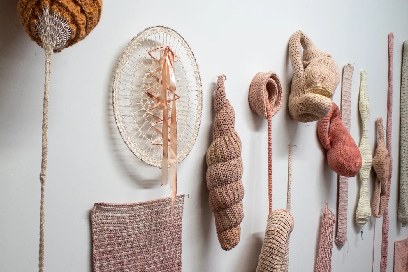 Ophelia Arc wall display of crocheted textile sculptures in flesh colors resembling skin and organic forms