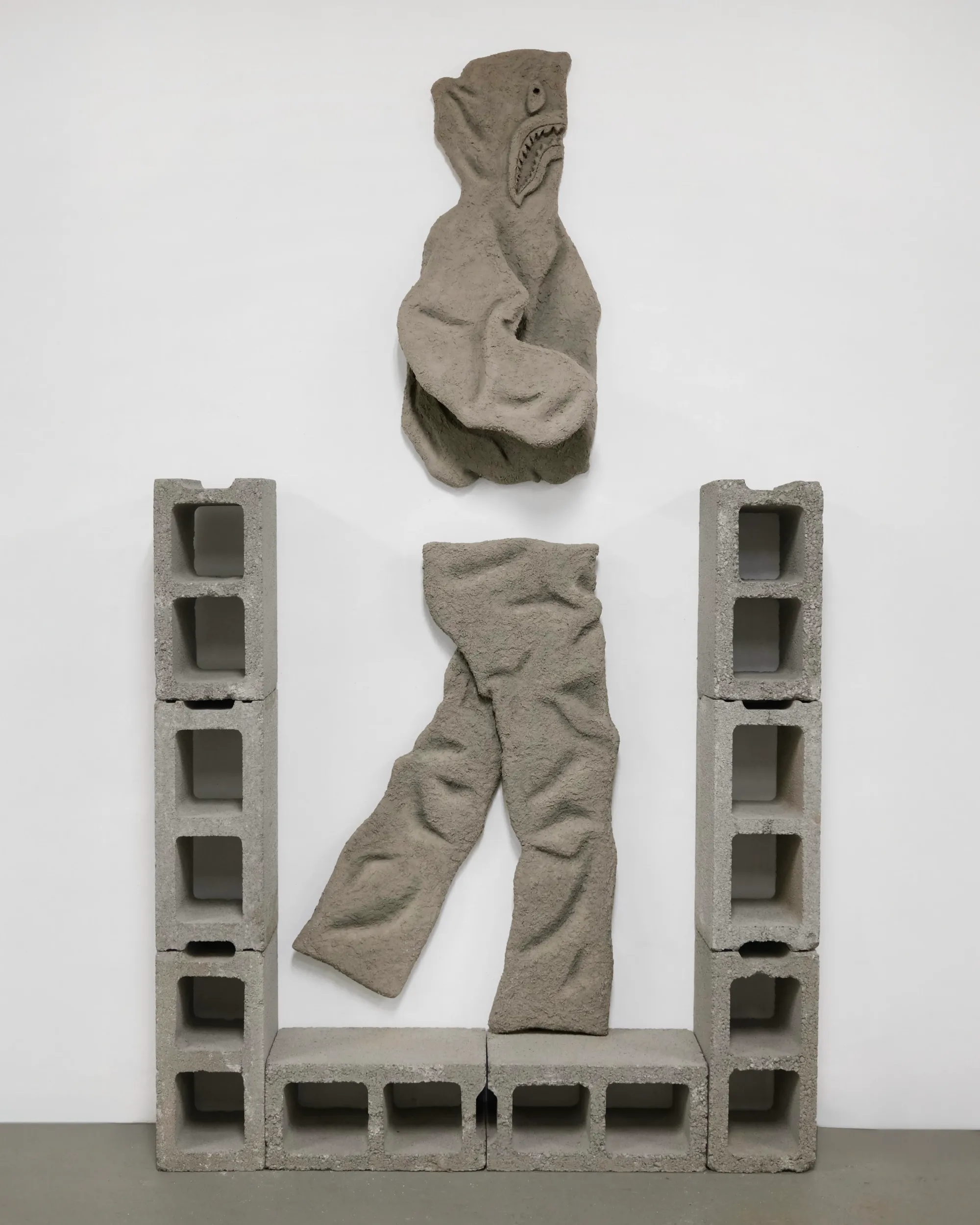 Daniel Castro sculpture: wall-mounted concrete hoodie and pants framed by cinder blocks, urban identity and authority.