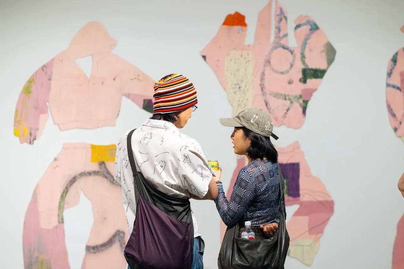 Visitors in front of cut-out garment paintings; gallery scene showing scale and audience engagement.