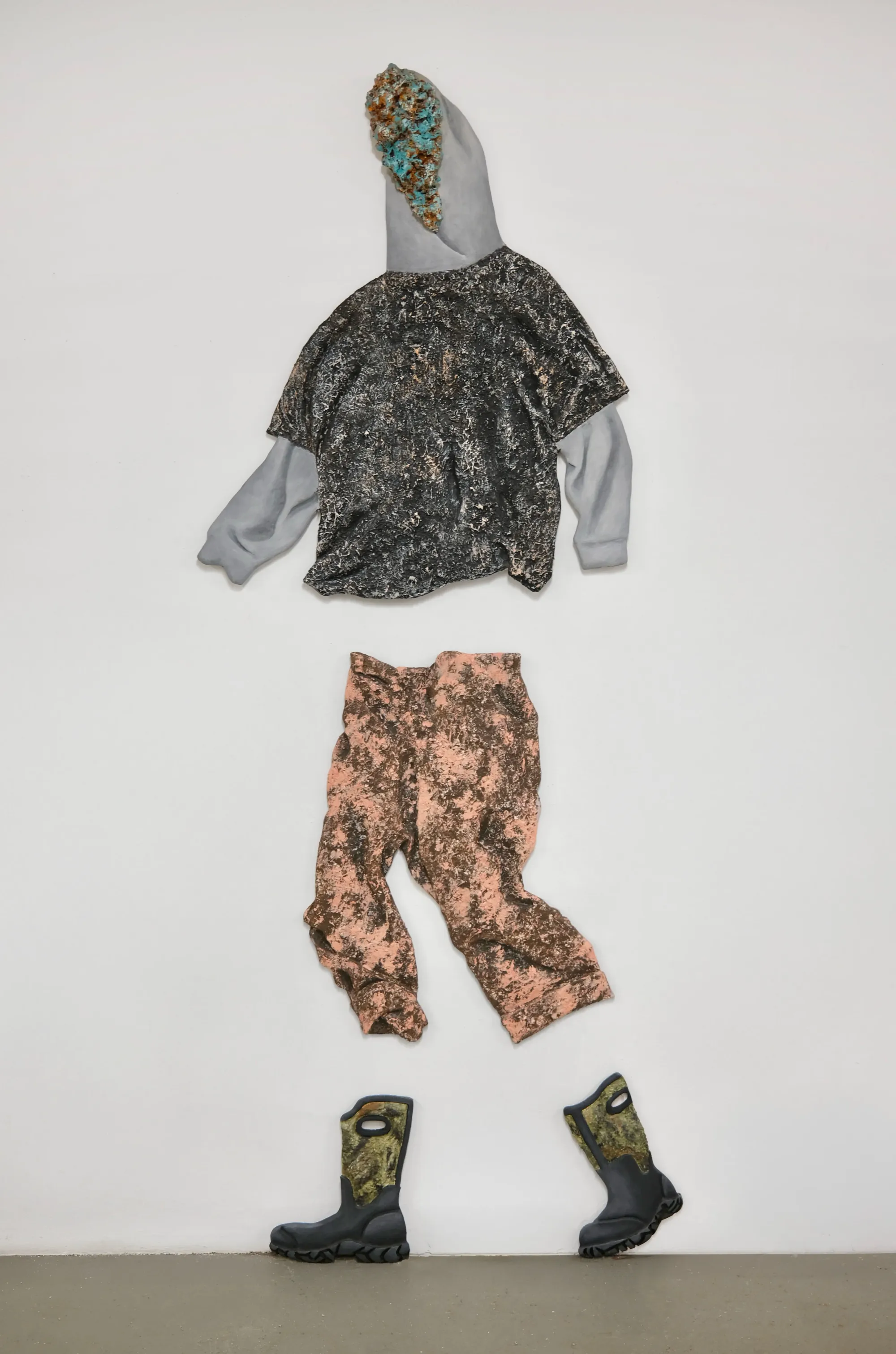 Hoodie, shirt, pants, and boots arranged as a wall relief with gritty textures; streetwear as object.