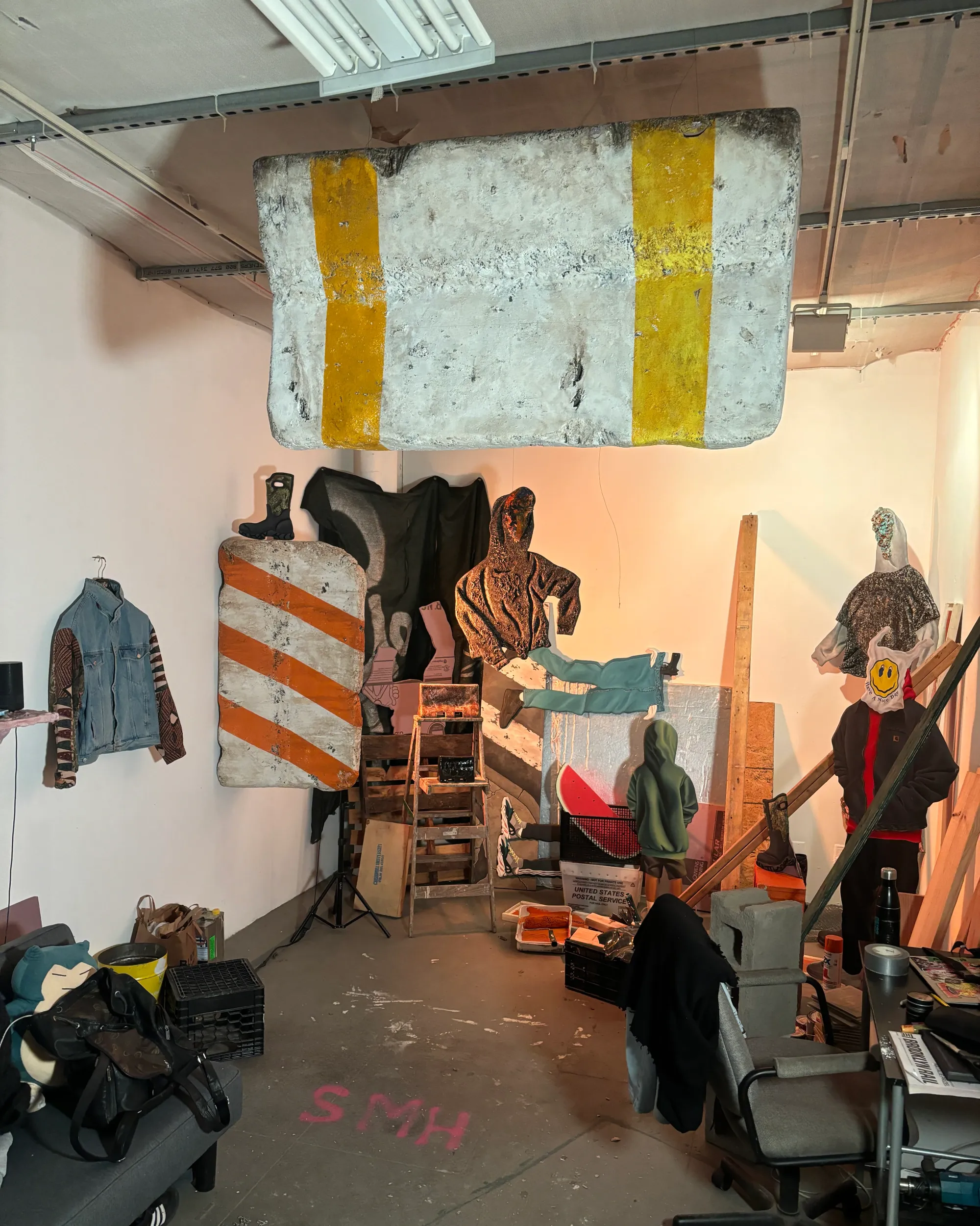 Daniel Castro studio view showing hoodie, barrier, and cone sculptures, plus a hanging panel with yellow stripes and works in progress.